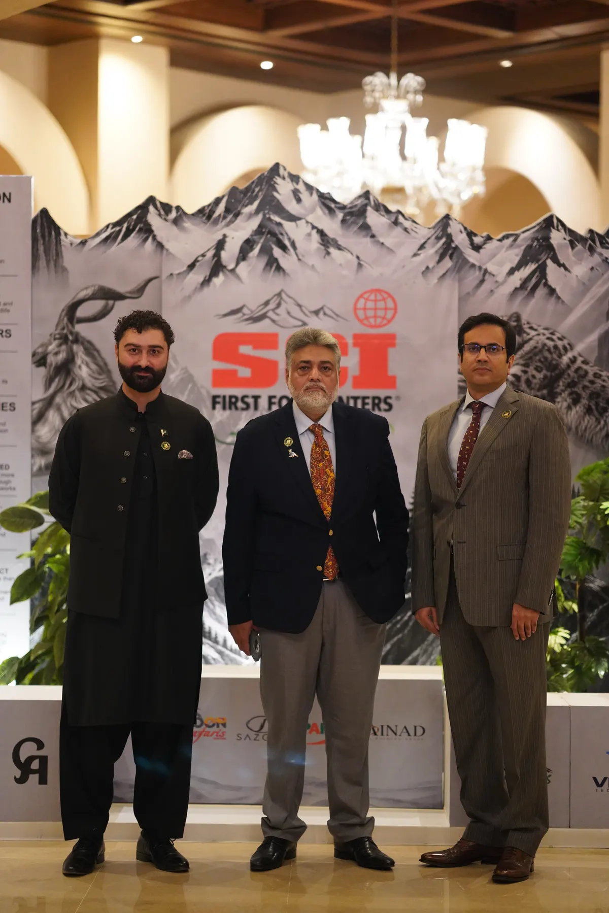 Three chapter members stand in front of a mountain backdrop bearing the SCI First For Hunters logo.