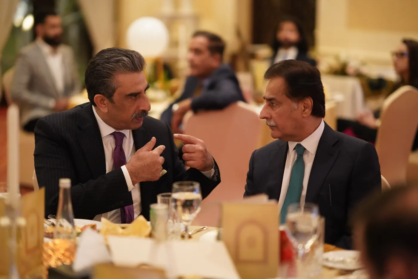 Two guests in conversation at a gala table, lit by candlelight.