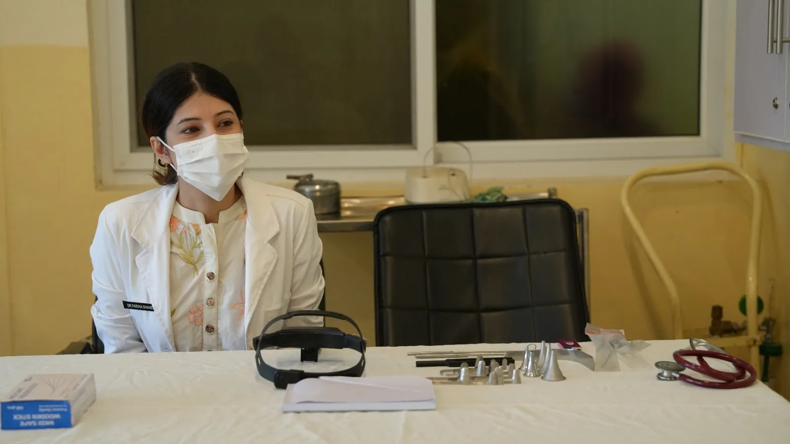 A woman doctor in a white coat sits at her desk waiting for patients.