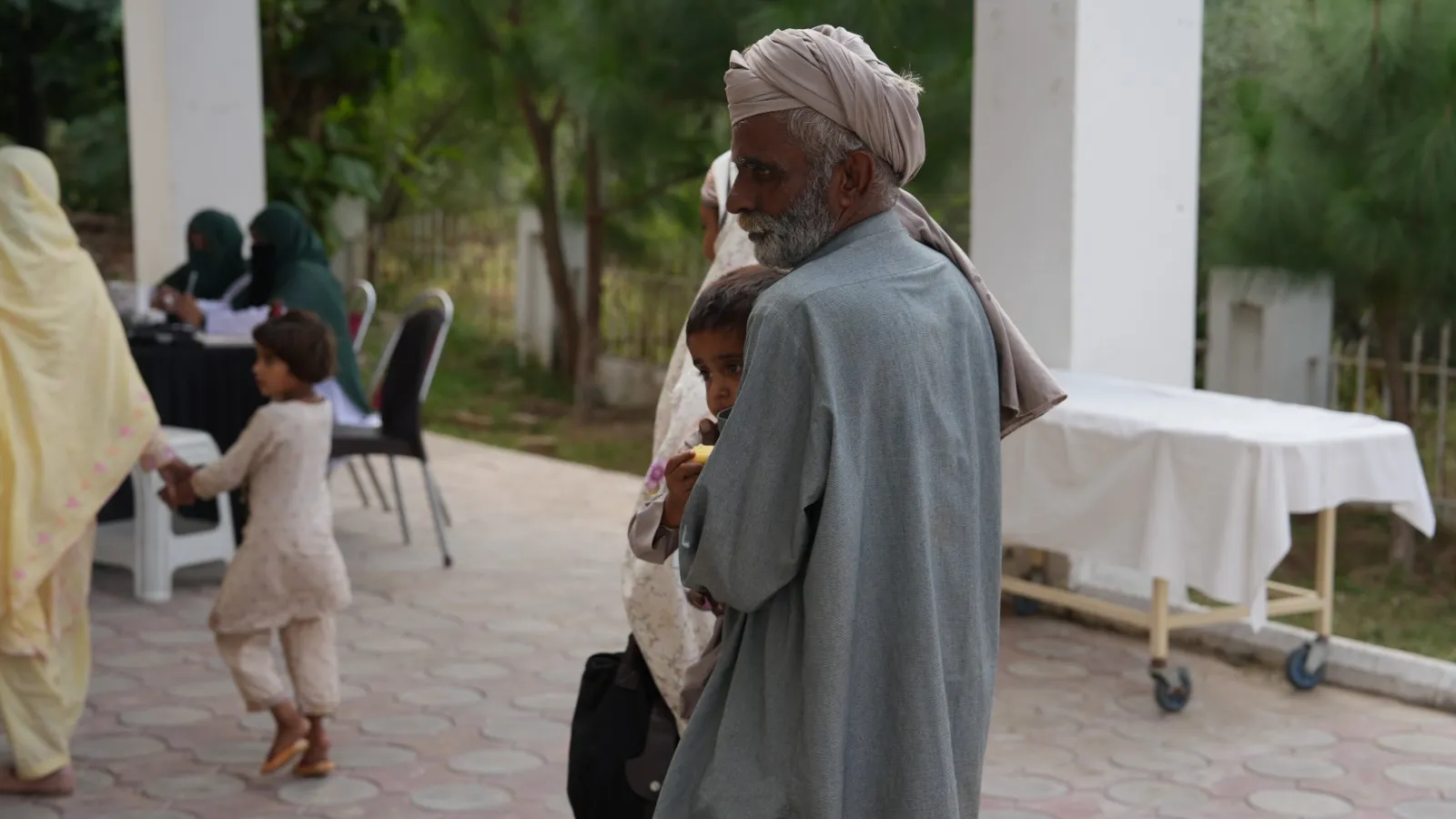 An elderly man in a turban arrives under the covered walkway as a child walks past.