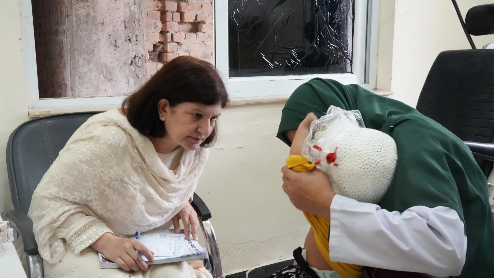 A woman doctor examines a child while a mother sits beside them.